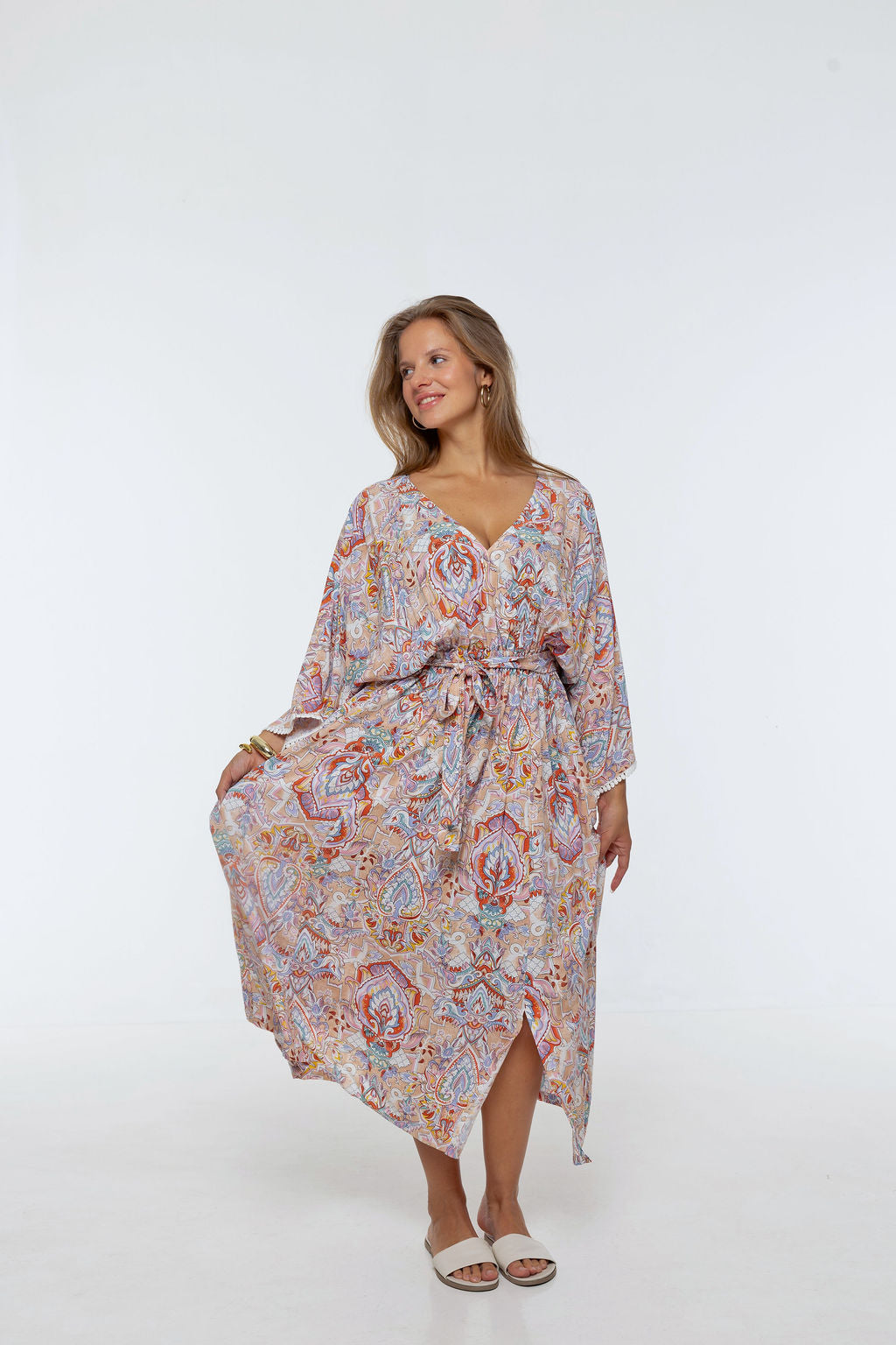 Woman wearing the Bianca Dress in Palazzo Print. A flowing dress with a wrap-over neckline, elasticated high waist, kimono sleeves and front split.
