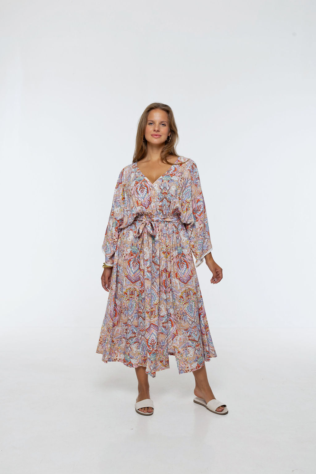 Woman wearing the Bianca Dress in Palazzo Print. A flowing dress with a wrap-over neckline, elasticated high waist, kimono sleeves and front split.