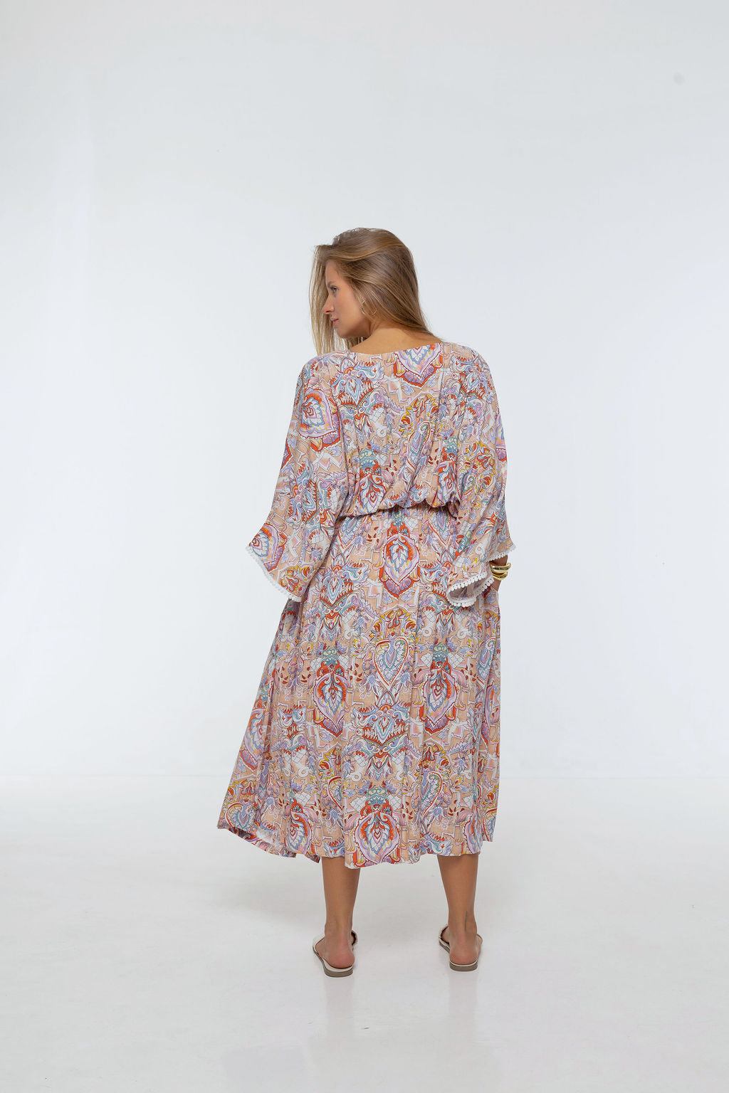 Woman wearing the Bianca Dress in Palazzo Print. A flowing dress with a wrap-over neckline, elasticated high waist, kimono sleeves and front split.