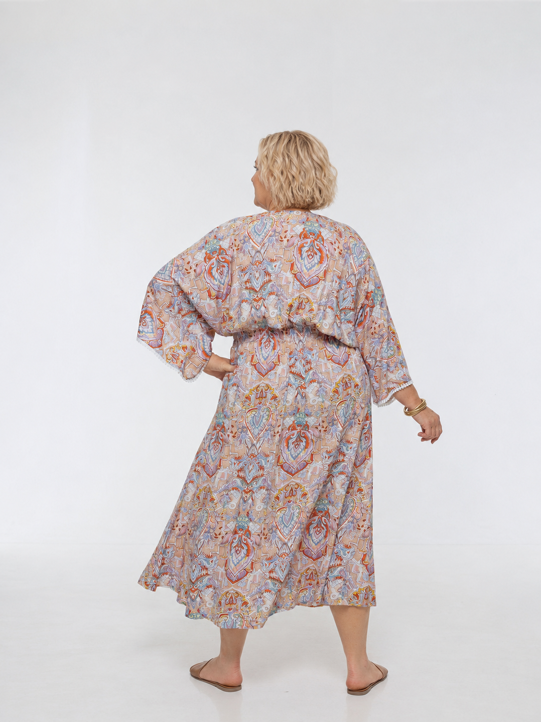 Woman wearing the Bianca Dress in Palazzo Print. A flowing dress with a wrap-over neckline, elasticated high waist, kimono sleeves and front split.