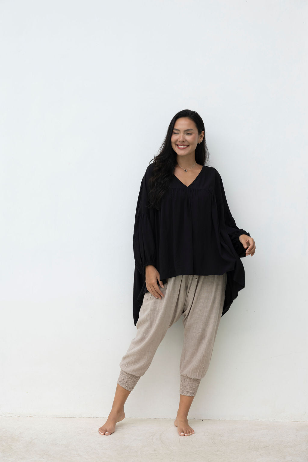Woman wearing a black top and beige pants against a white background