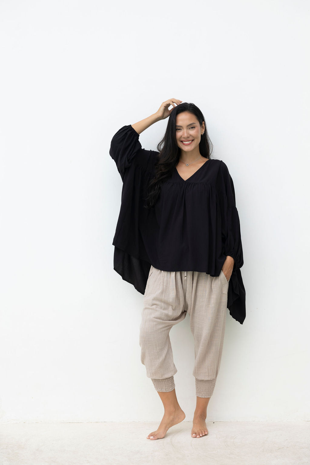 Woman wearing a black top and beige pants against a white background