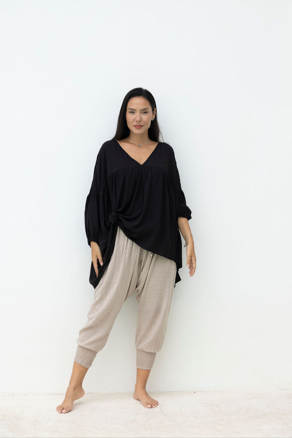 Woman wearing a black top and beige pants against a white background