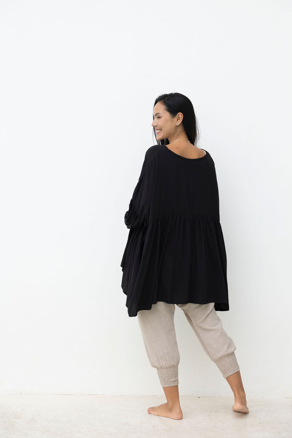 Woman wearing a black oversized sweater and beige pants on a white background