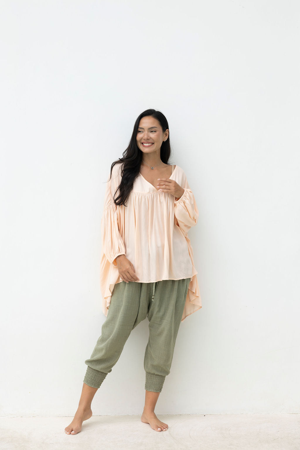 Woman wearing a blush top and light green pants against a white background
