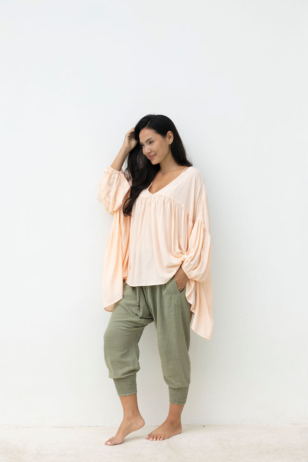 Woman wearing a blush top and light green pants against a white background