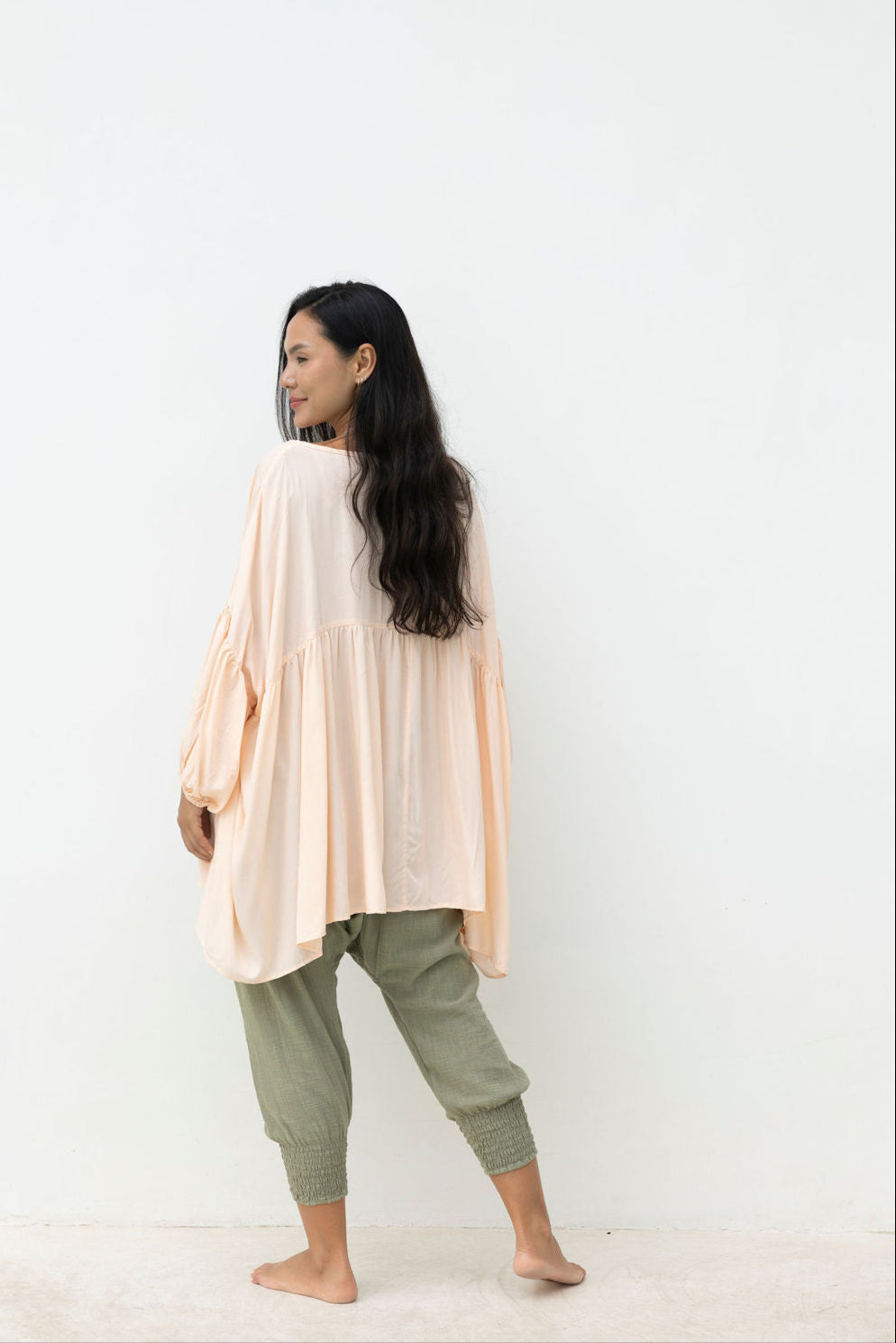 Woman wearing a blush top and light green pants against a white background