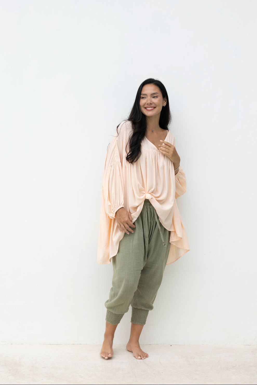Woman wearing a blush top and light green pants against a white background