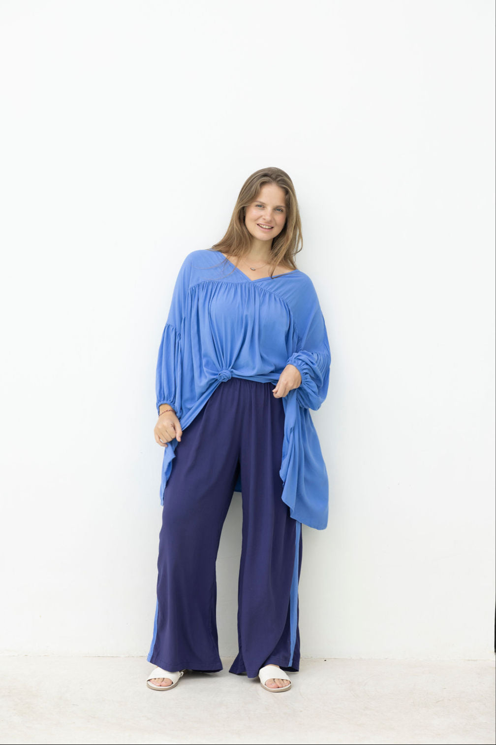 Woman wearing a blue top and dark blue pants against a white background