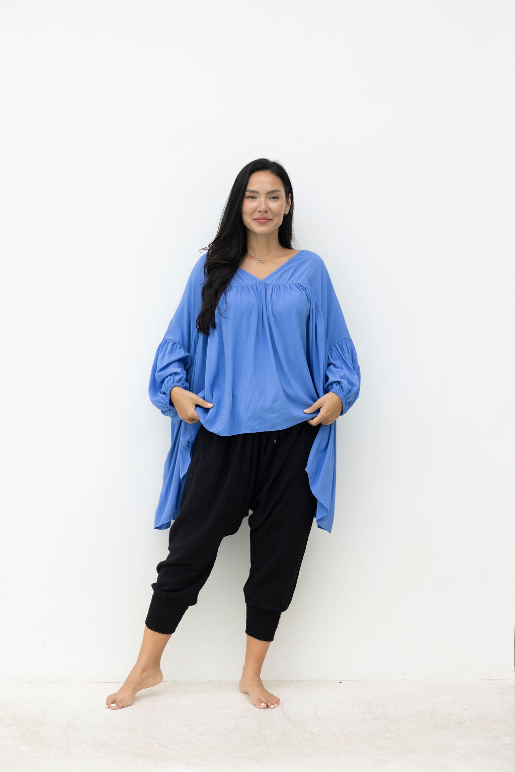 Woman wearing a blue oversized top and black pants against a white background