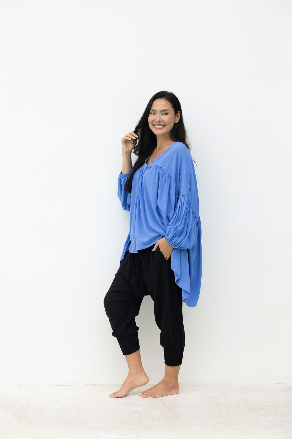 Woman wearing a blue oversized top and black pants against a white background