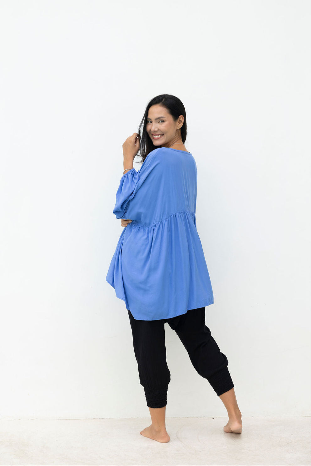 Woman wearing a blue long-sleeve top and black pants on a white background