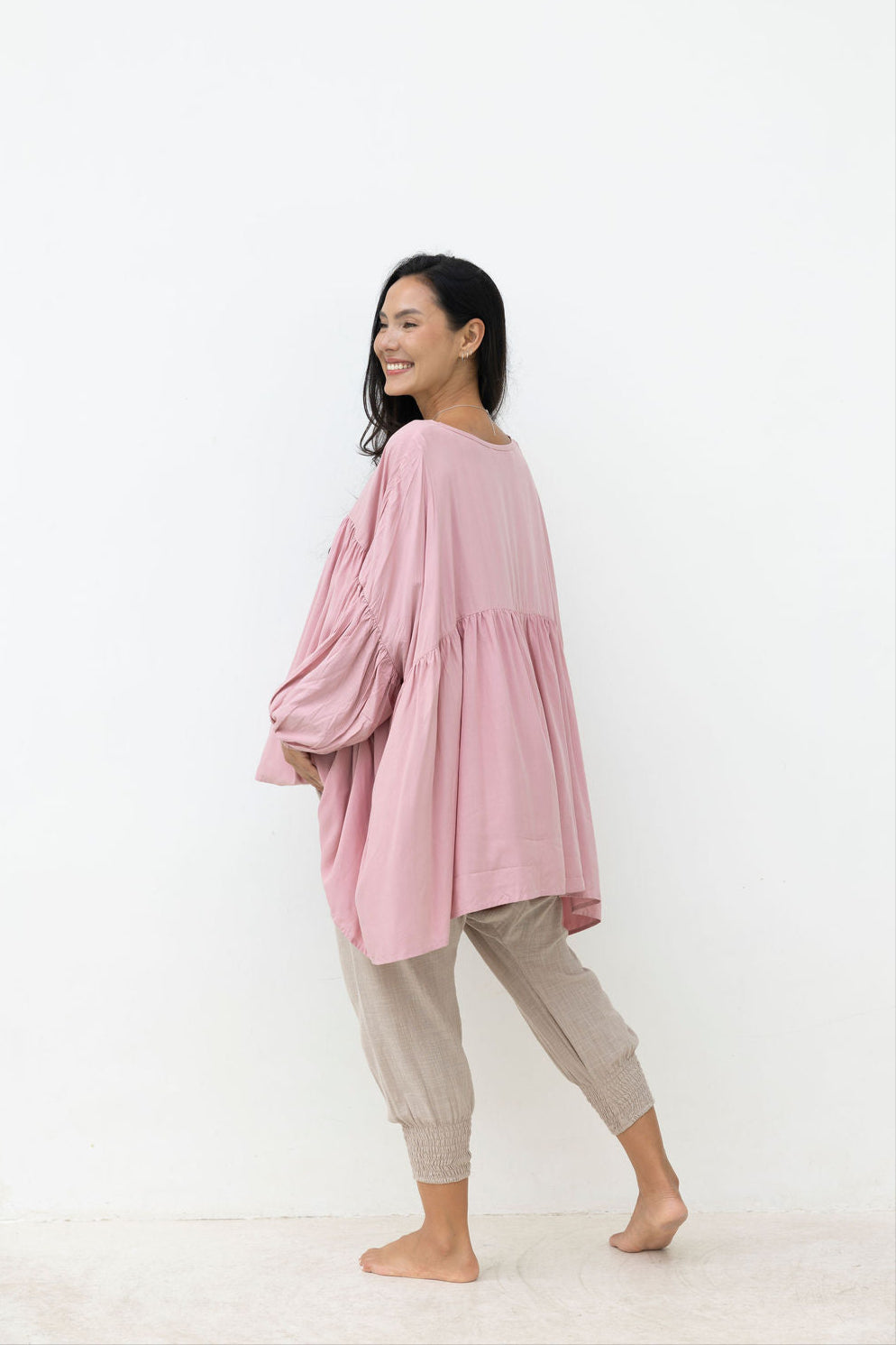 Woman wearing a pink oversized top and beige pants on a white background