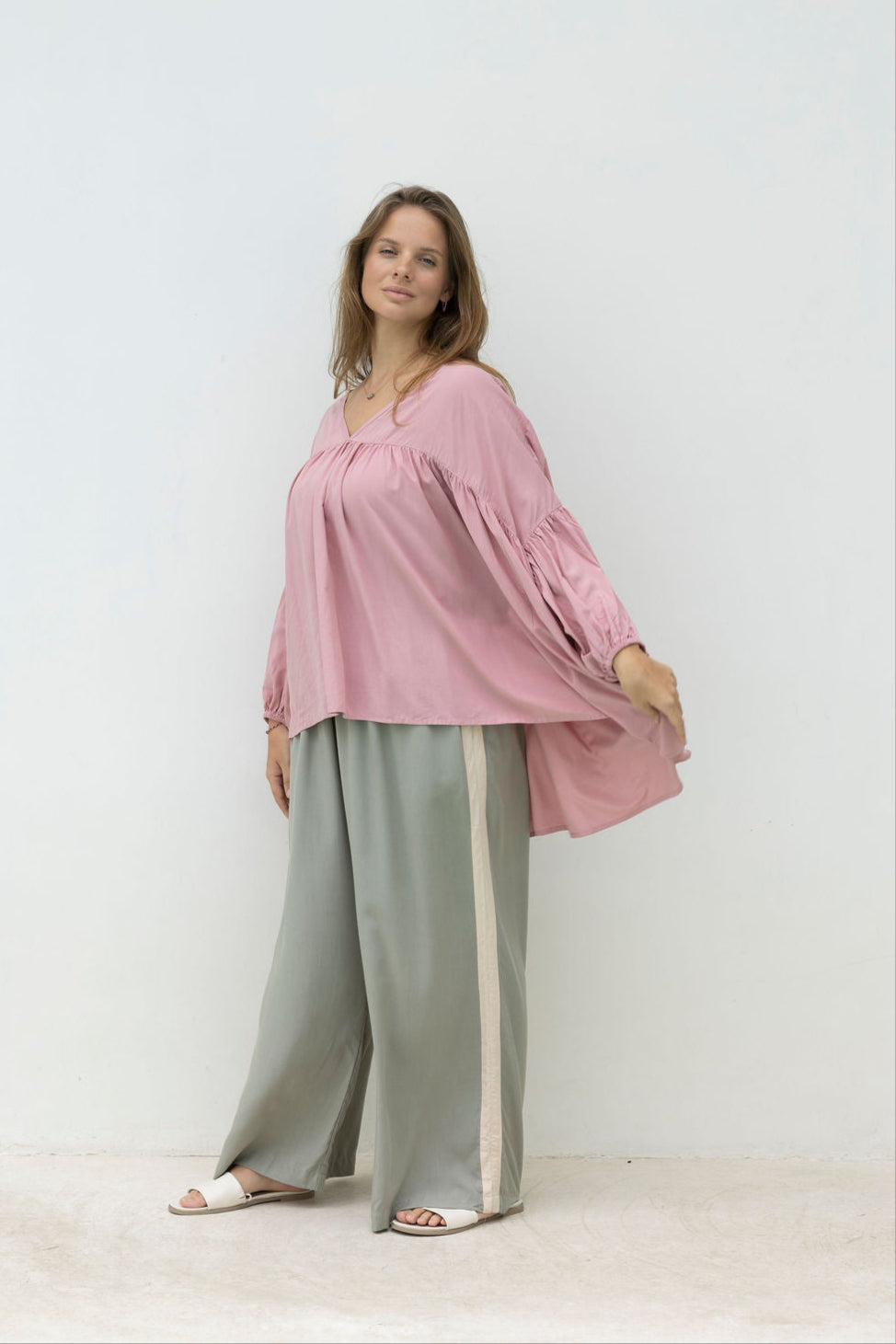 Woman wearing a pink blouse and light green pants against a white background