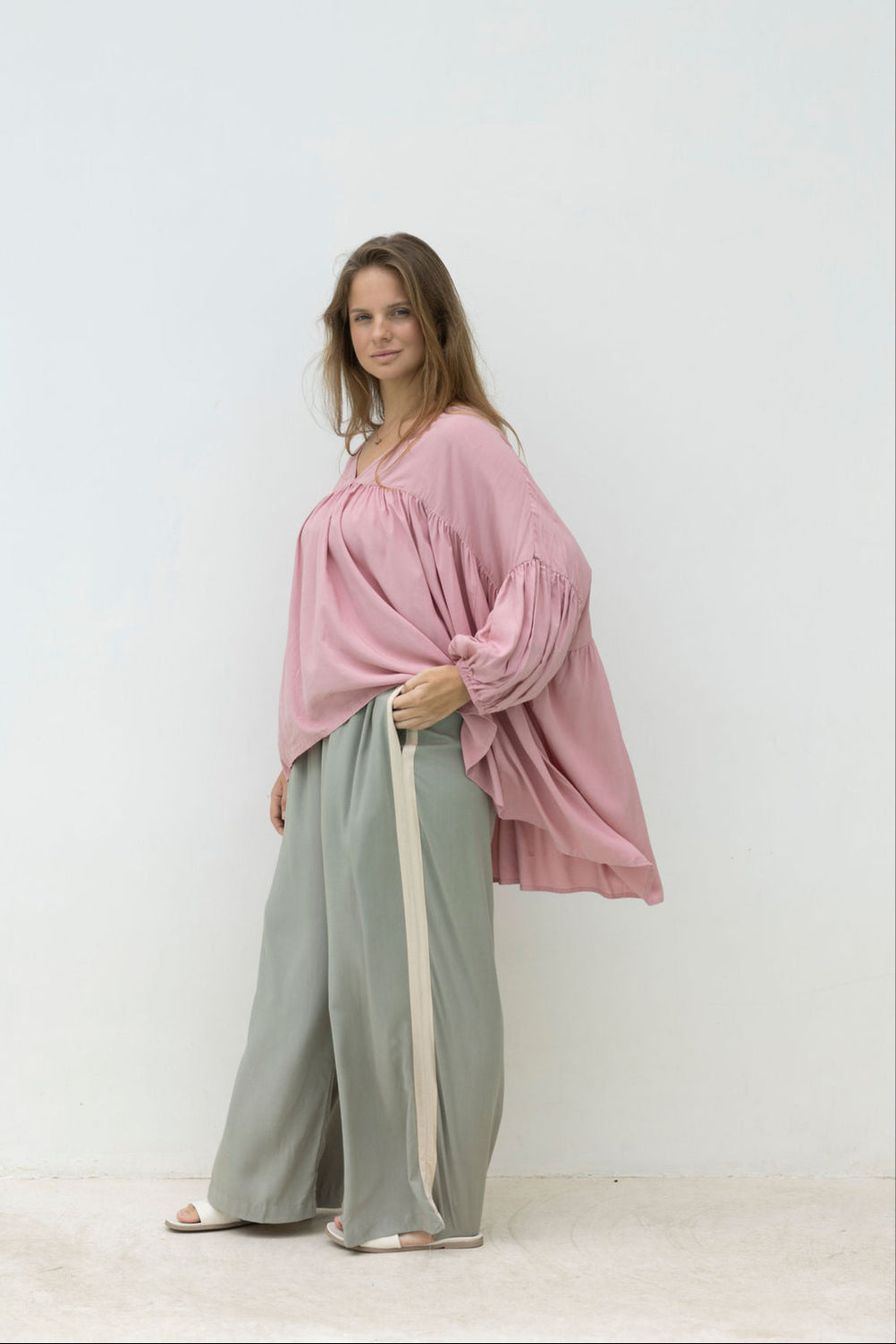 Woman wearing a pink blouse and light green pants against a white background