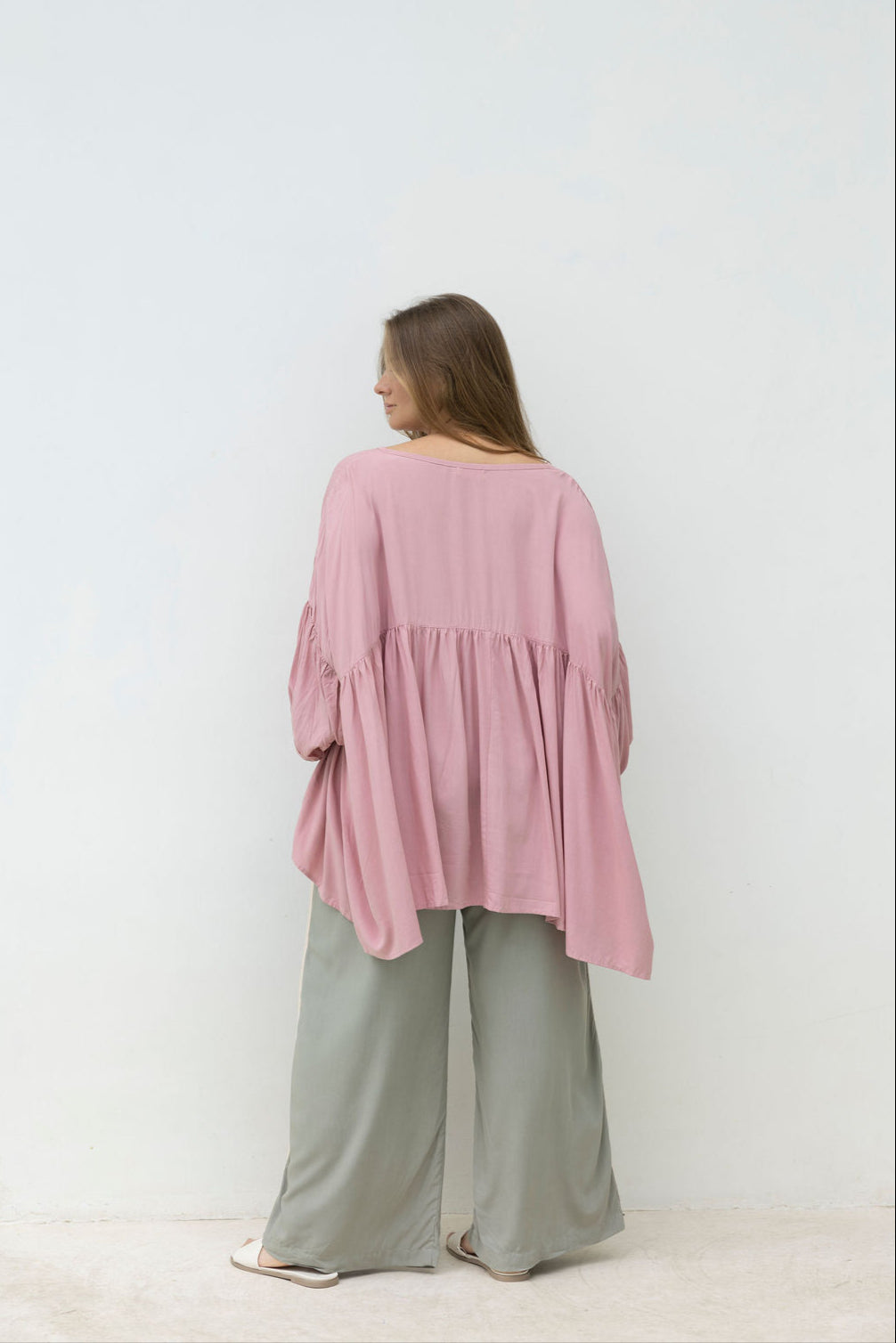 Woman wearing a pink blouse and light green pants against a white background