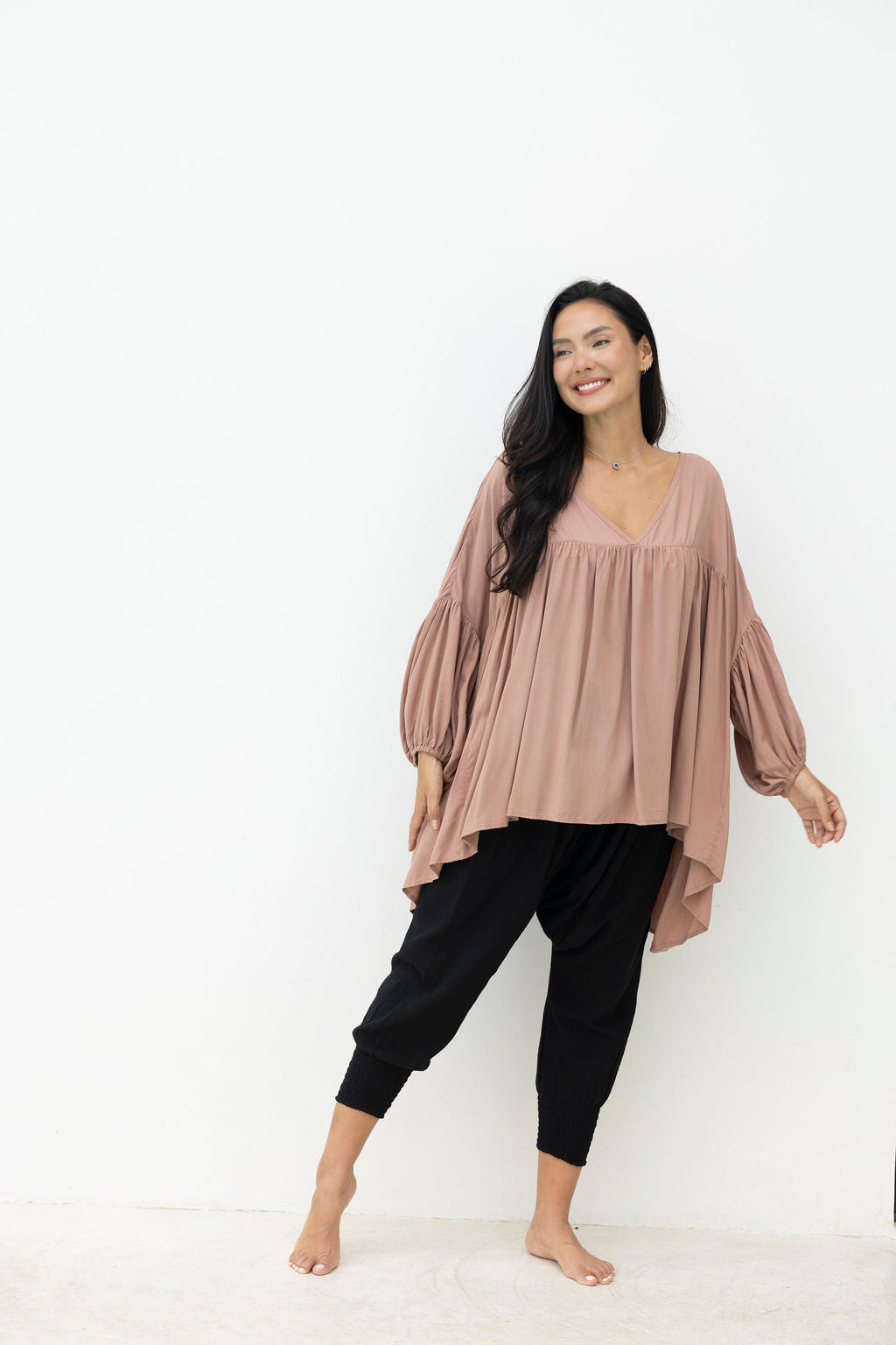 Woman wearing a mocca blouse and black pants against a white background