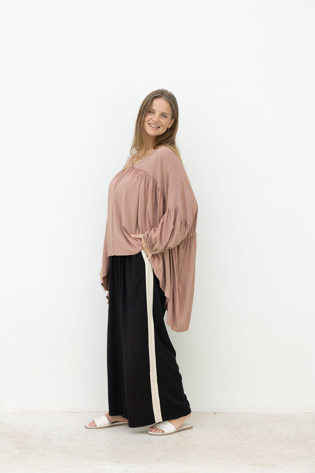 Woman wearing a mocca blouse and black pants against a white background