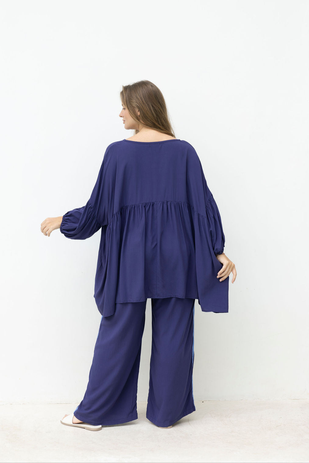 Woman wearing a long navy top with a pant with a blue stripe on the side on a white background