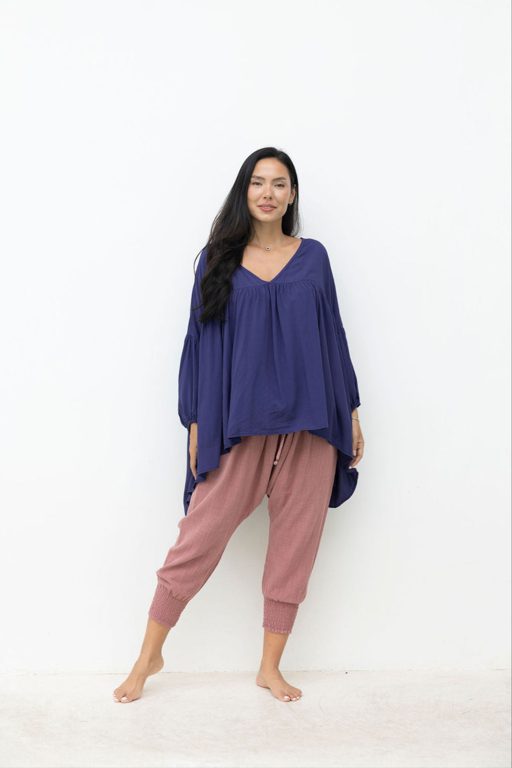 Woman wearing a long navy top with a dusty pink pant on a white background