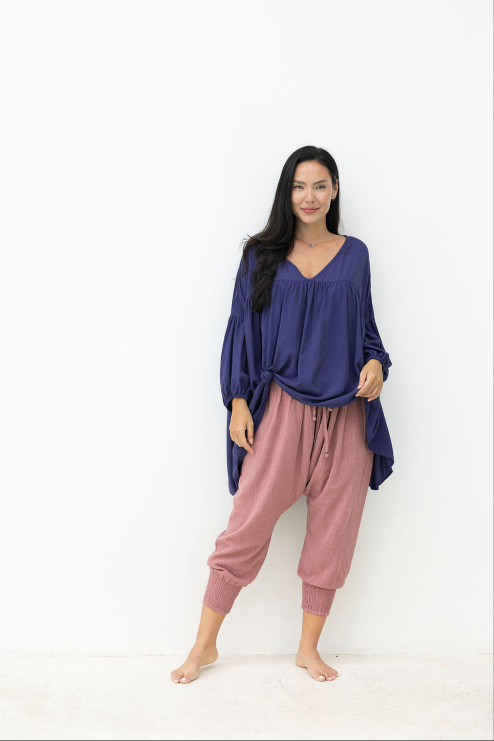 Woman wearing a long navy top with a dusty pink pant on a white background