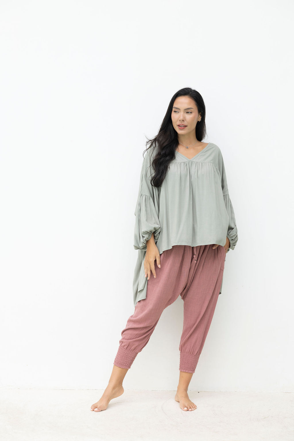 Woman wearing a light green top and pink pants on a white background