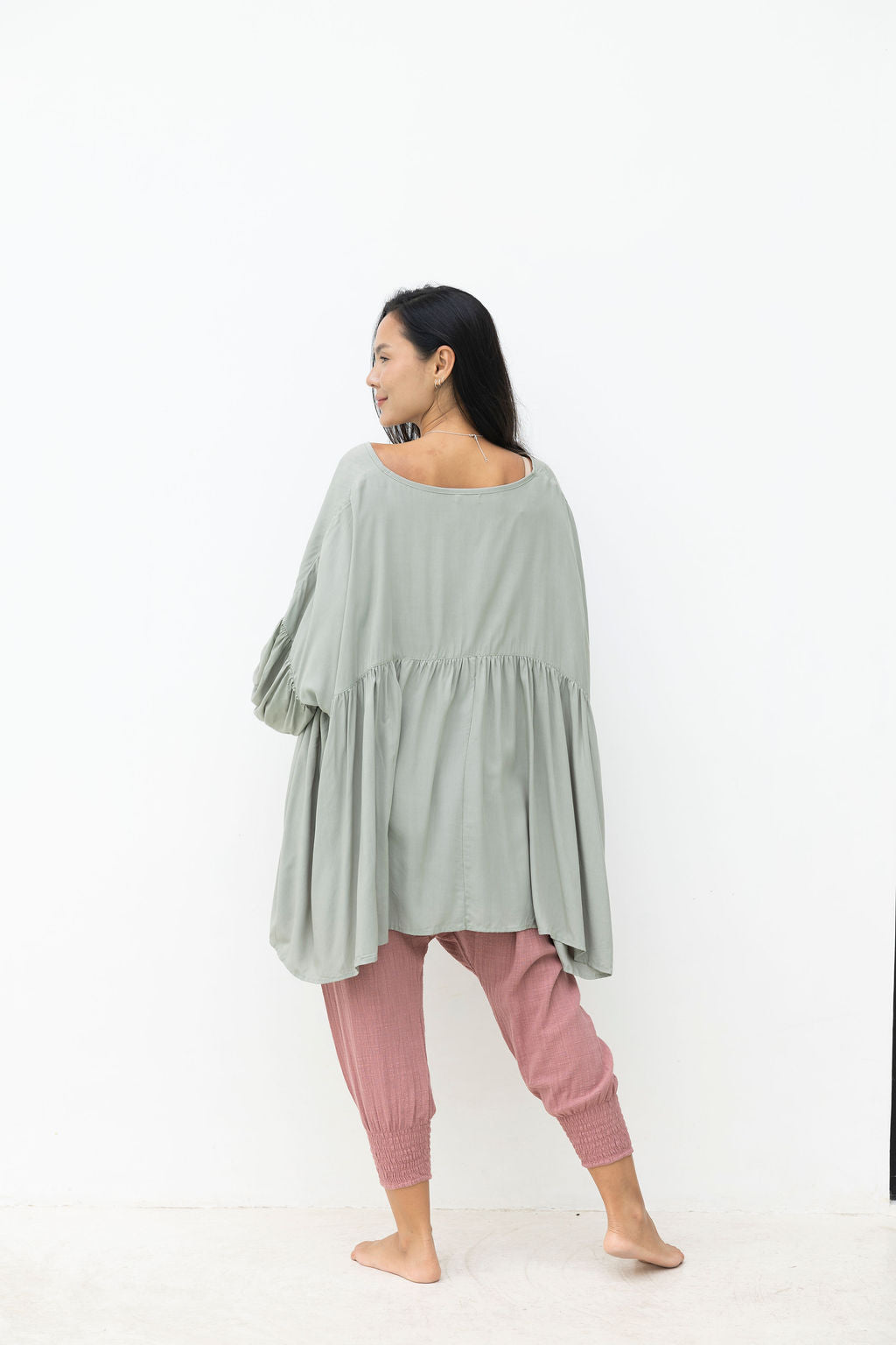 Woman wearing a light green top and pink pants on a white background
