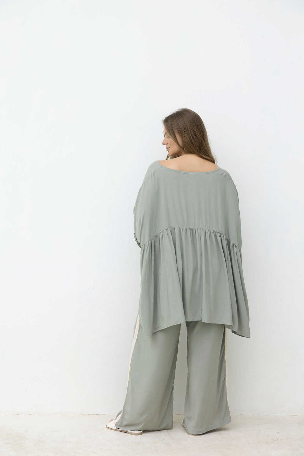 Woman wearing a light green off-shoulder top and wide-leg pants against a white background