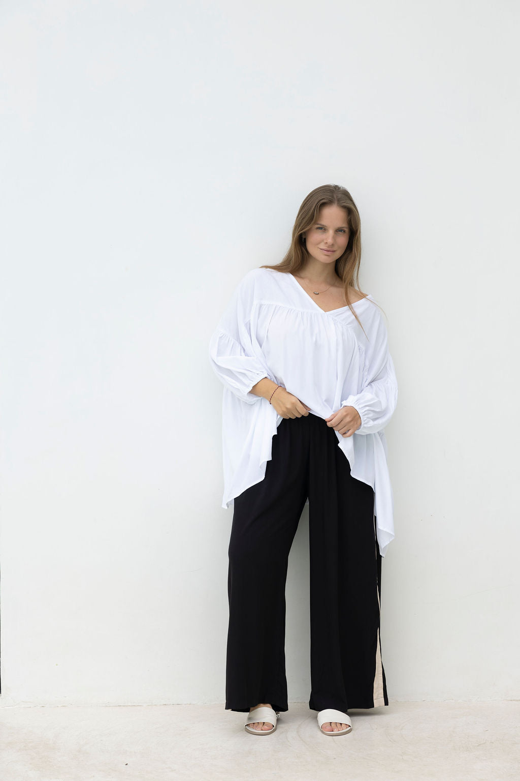 Woman wearing a white oversized shirt and black pants against a white background