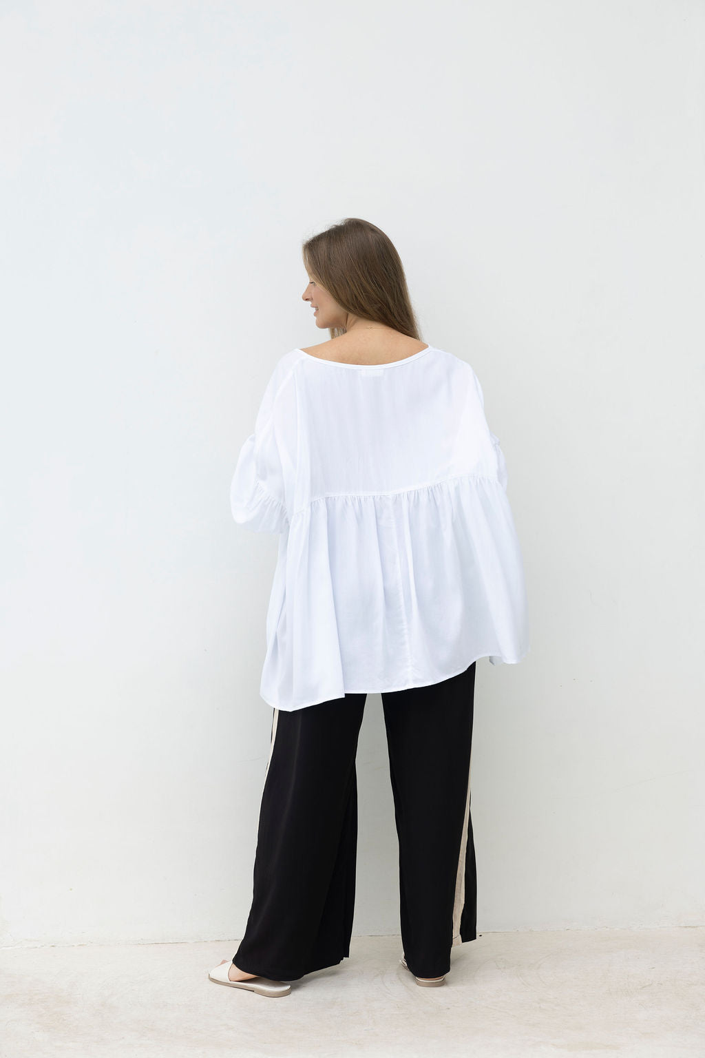 Woman wearing a white blouse and black pants against a white background
