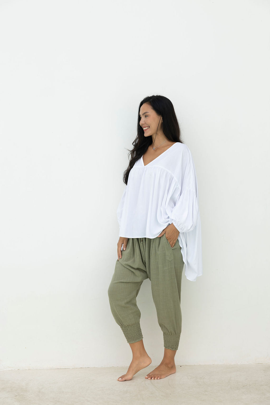 Woman wearing a white blouse and green pants against a white background
