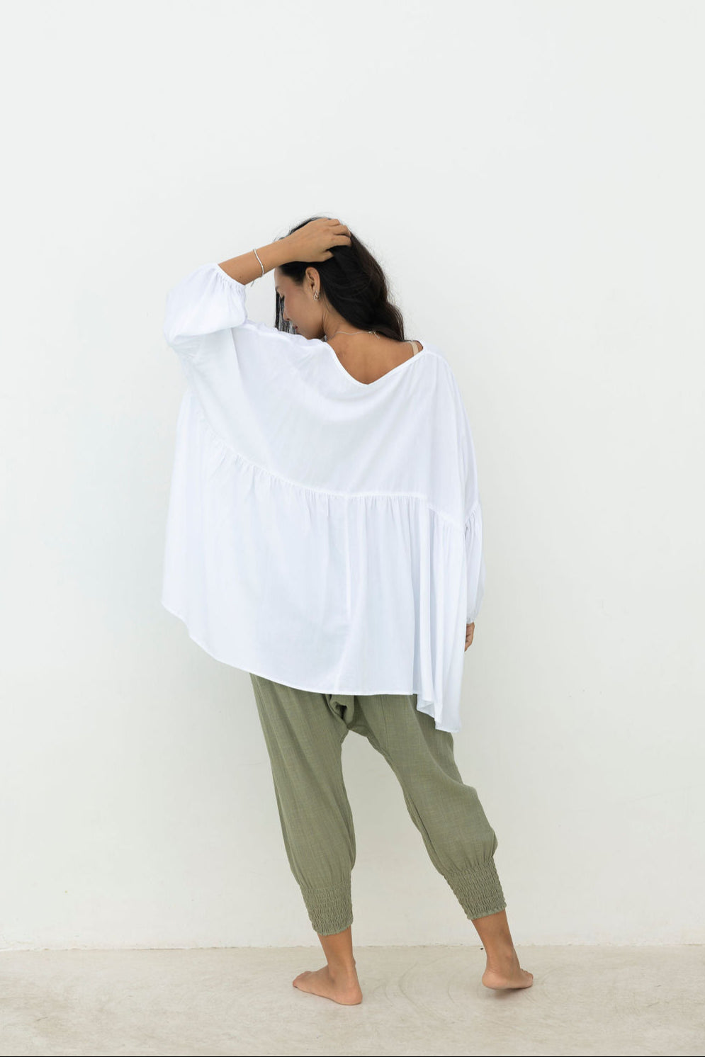 Person wearing a white oversized top and green pants against a plain background