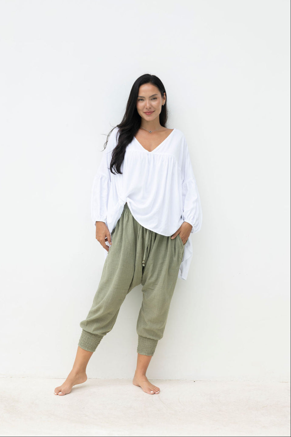 Woman wearing a white top and green pants against a white background