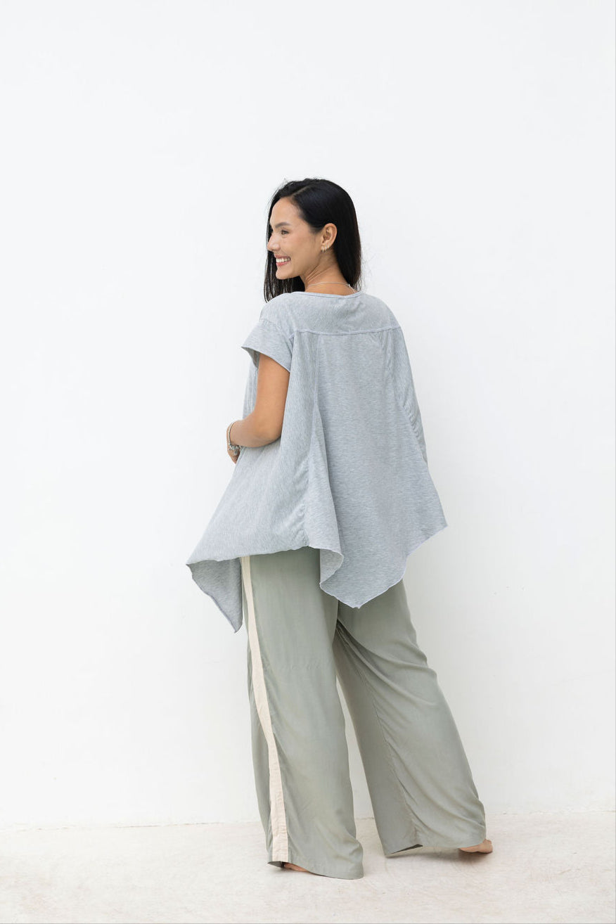 Woman wearing a light gray top and pants standing against a white background