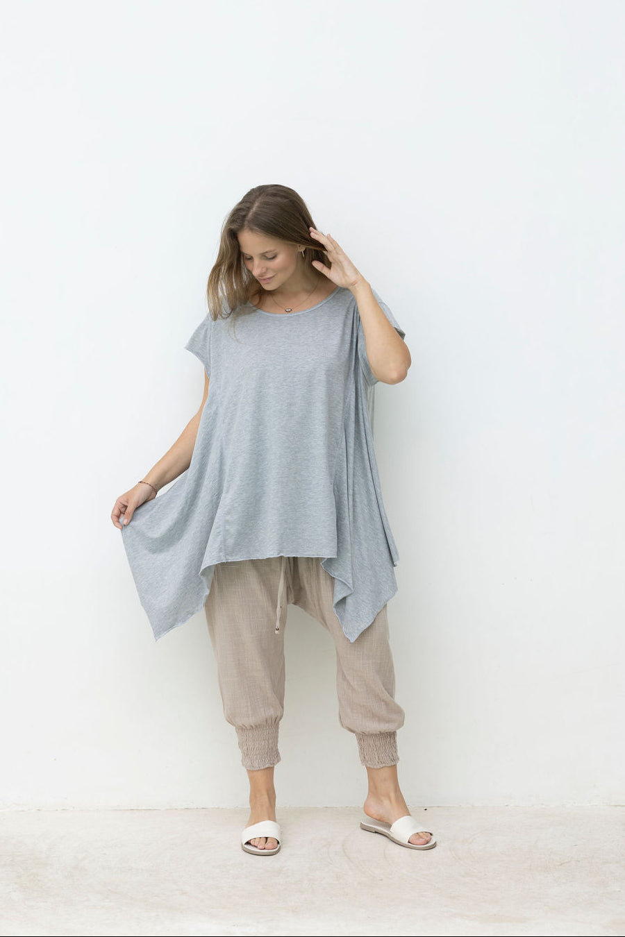 Woman wearing a light blue oversized top and beige pants against a white wall.