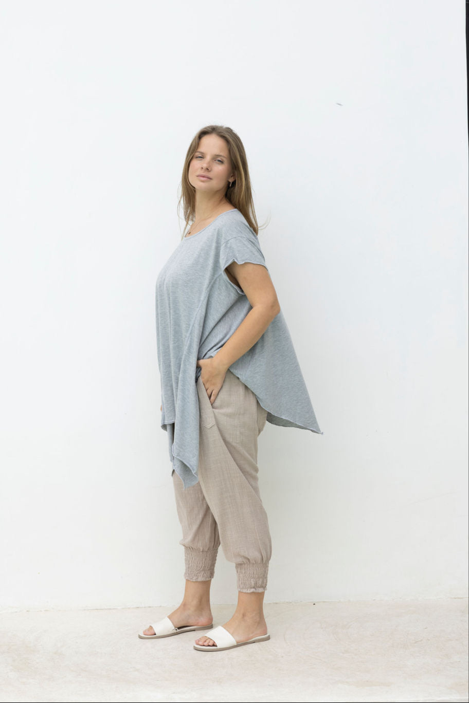 Woman wearing a light blue top and beige pants standing against a white background