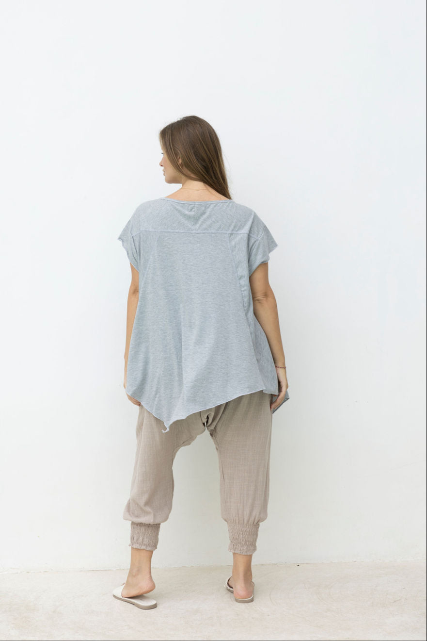Woman wearing a light blue t-shirt and beige pants standing in front of a mirror on a white background