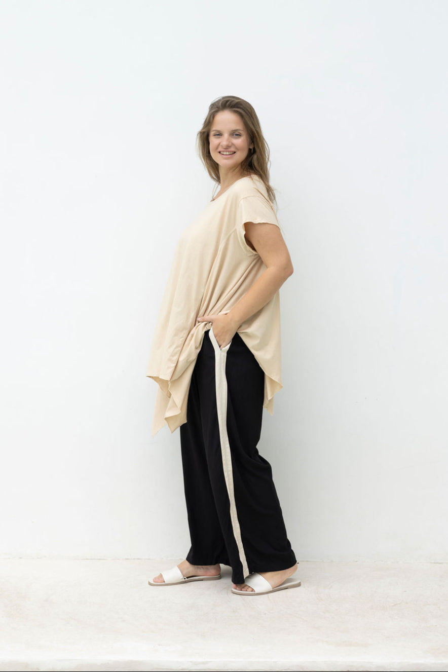 Woman wearing a beige top and black pants with white stripes against a white wall.
