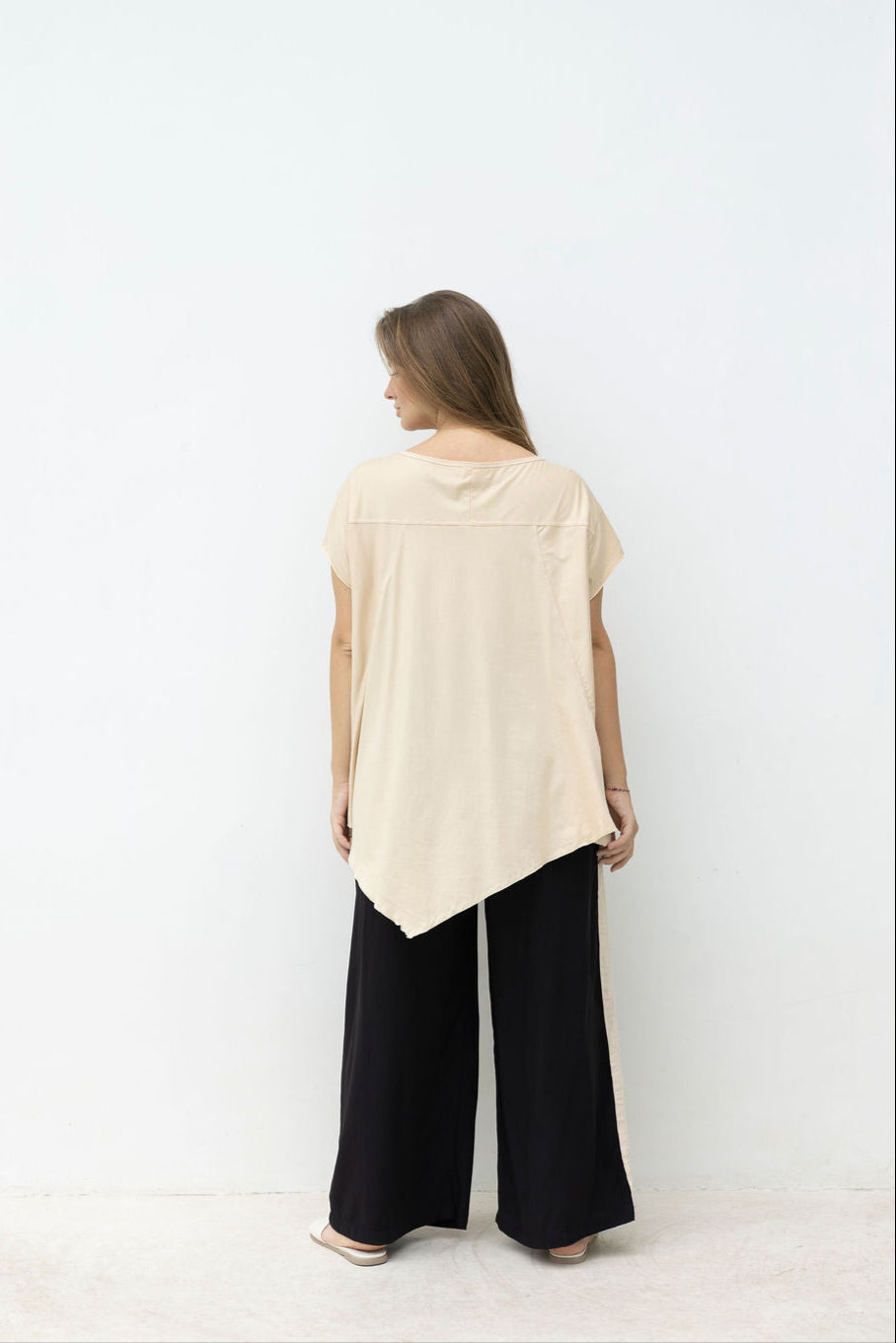 Woman wearing a beige sleeveless top and black pants standing in front of a mirror on a white background