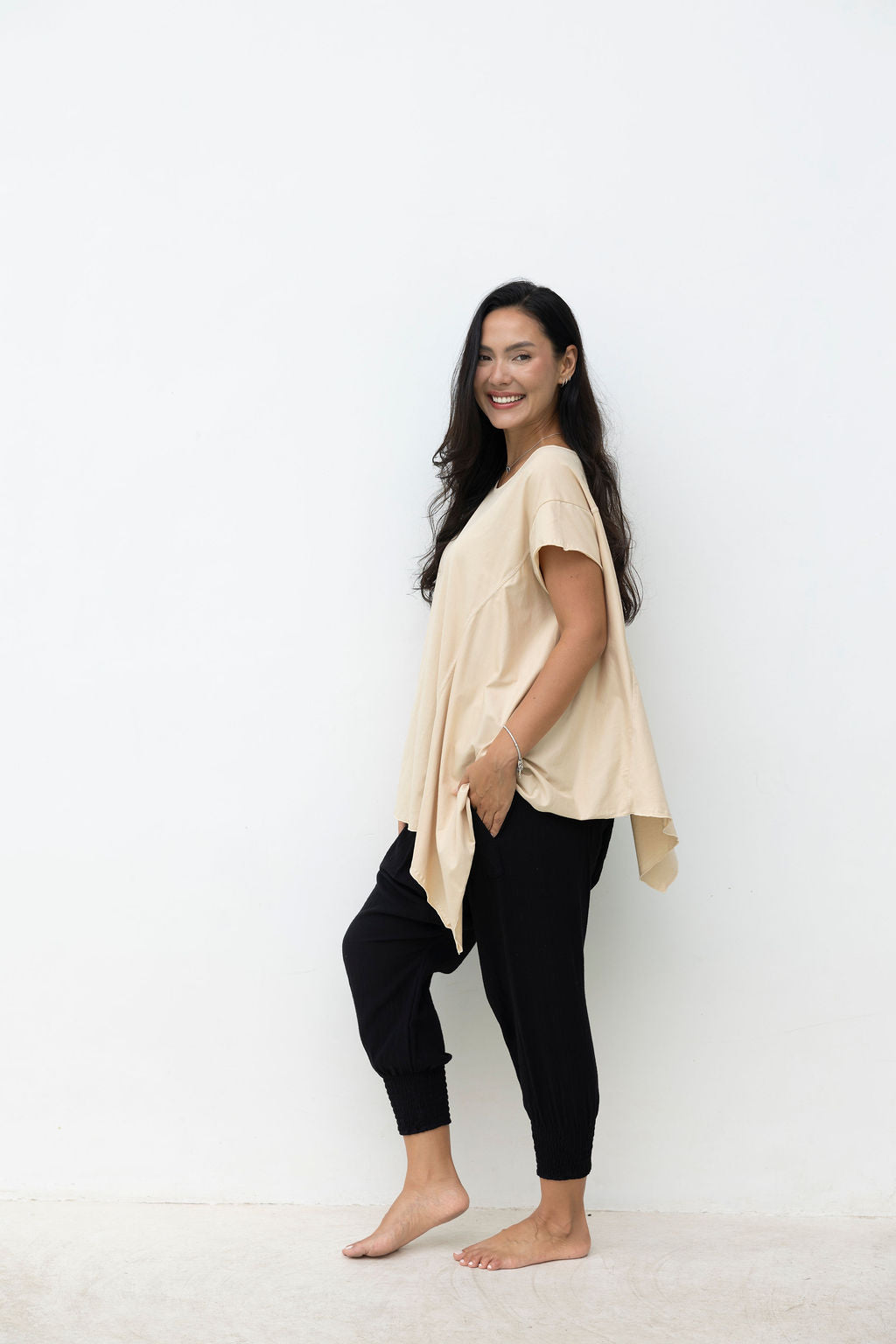 Woman wearing a beige top and black pants against a white background