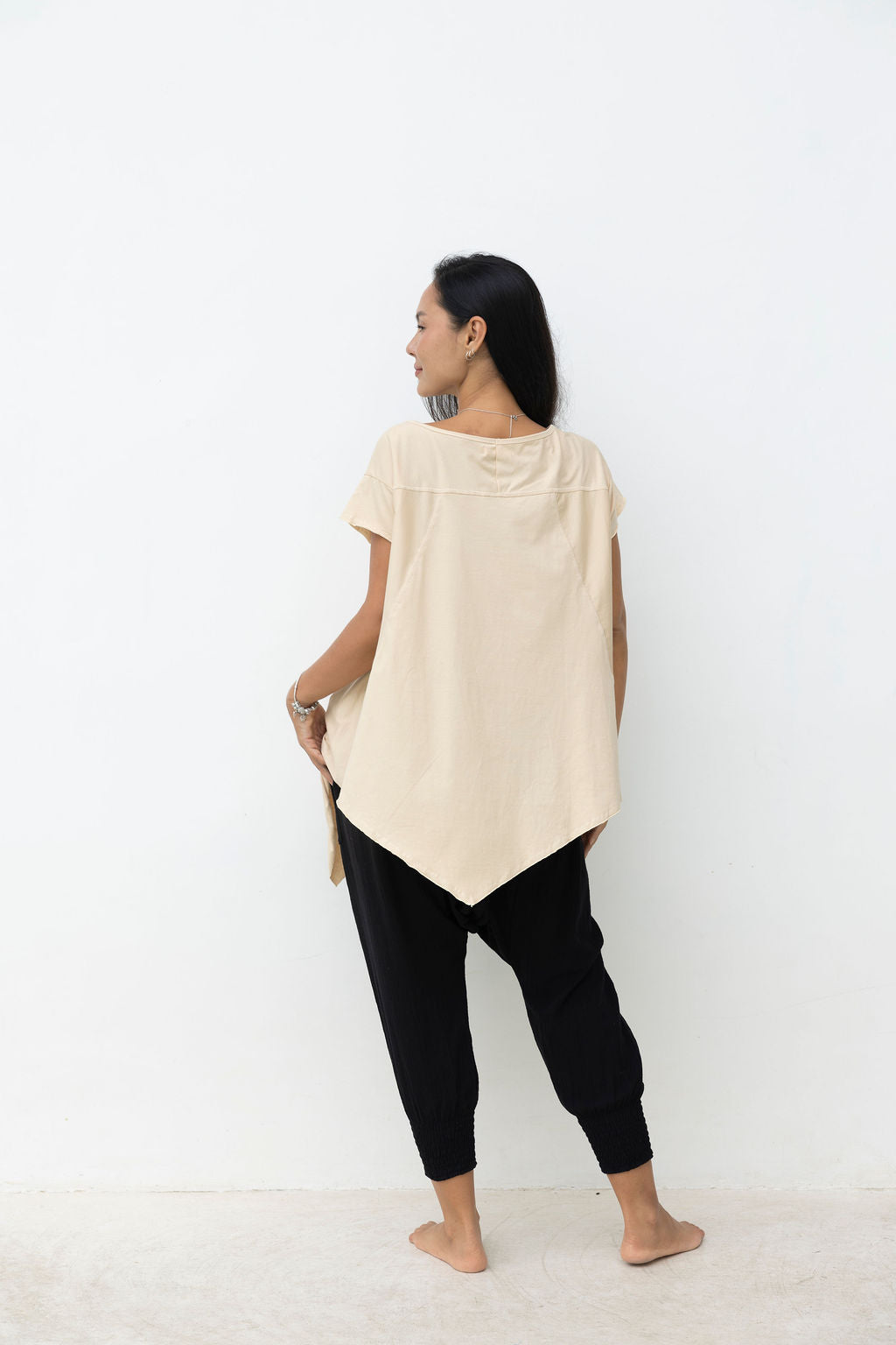 Woman wearing a beige tunic and black pants against a white background