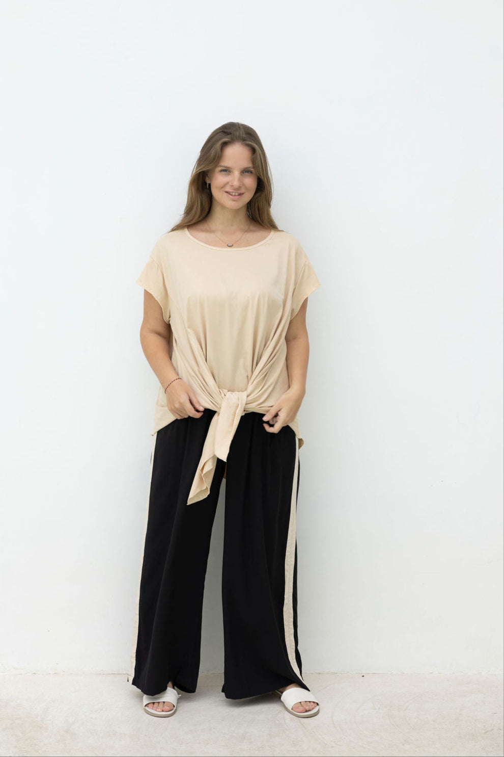 Woman wearing a beige top and black pants with white stripes against a white background