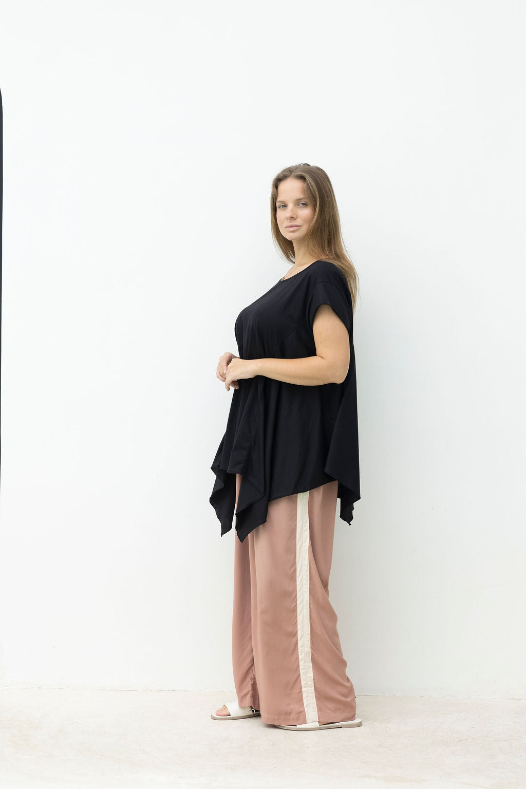 Woman wearing a black top and pink pants with a white stripe on a white background
