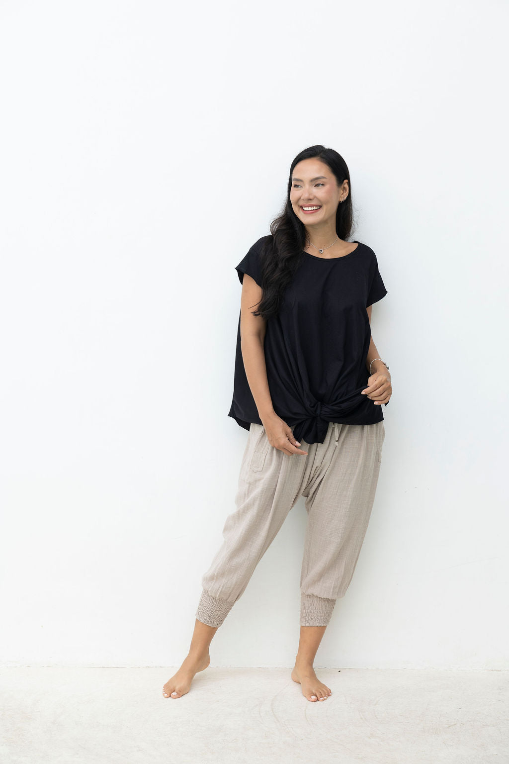 Woman wearing a black top and beige pants against a white background