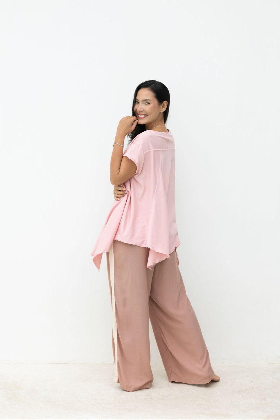 Woman wearing a pink top and brown pants against a white background