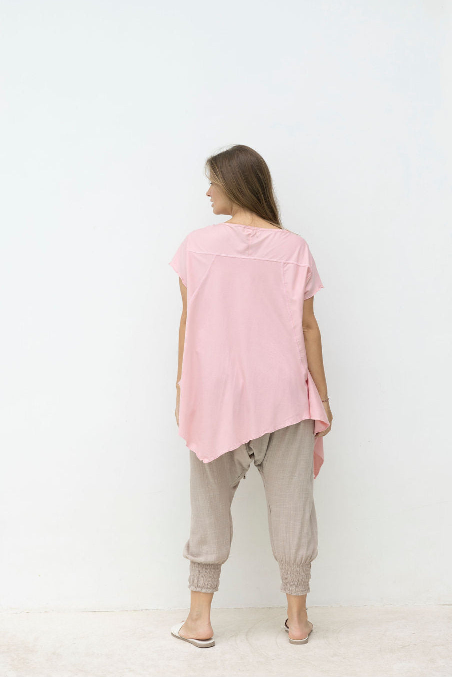 Woman wearing a pink top and beige pants against a white wall