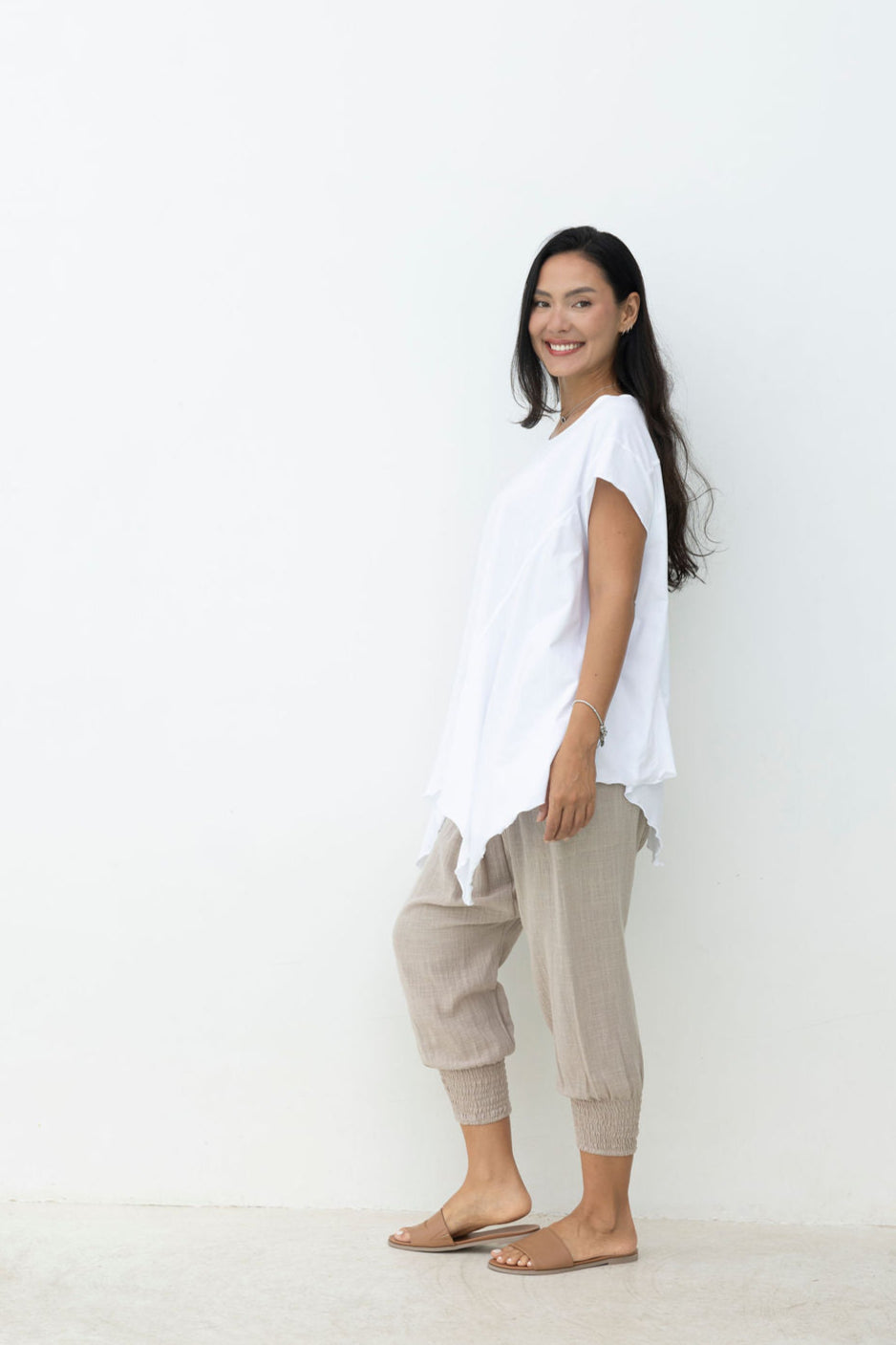Woman wearing a white t-shirt and beige pants standing against a white background