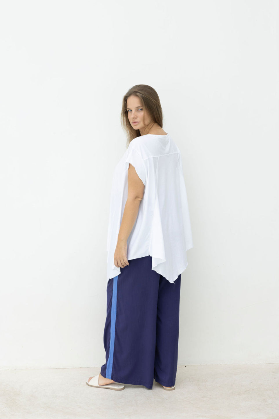 Woman wearing a white top and blue pants with a stripe against a white background