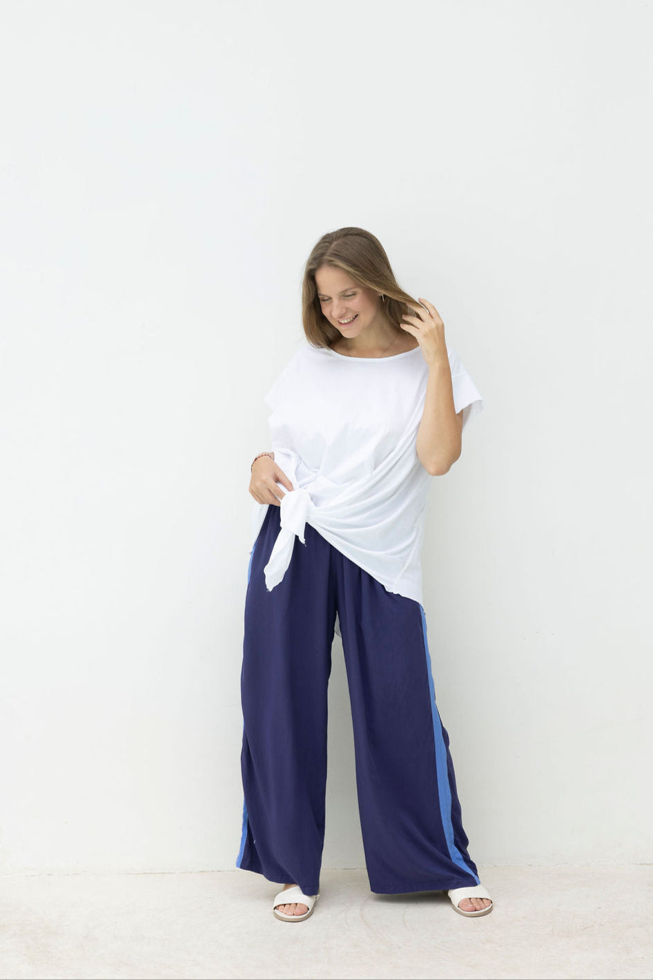 Woman wearing a white top and blue pants against a white wall