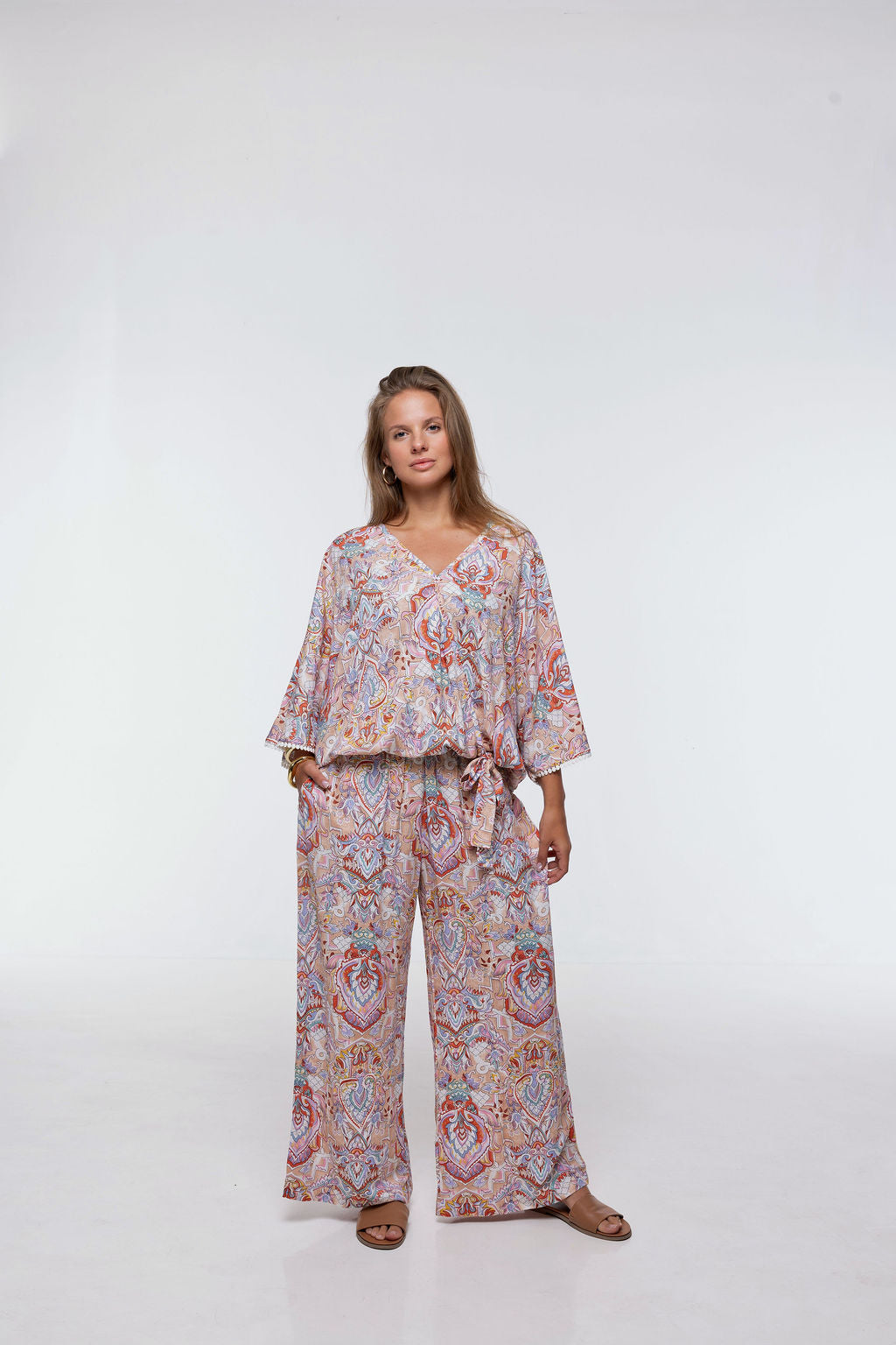 Woman wearing the Messina Top - Palazzo Print. A flowing printed rayon top with a wrap-over neckline, kimono sleeves, crochet trim, elastic waist with adjustable tie